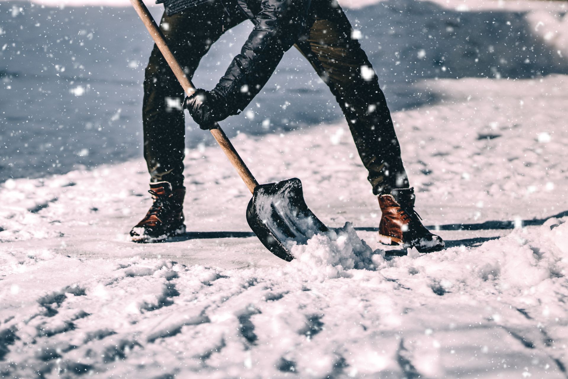 Young caucasian adult cleaning snow from sidewalk and using snow shovel after heavy snowstorm